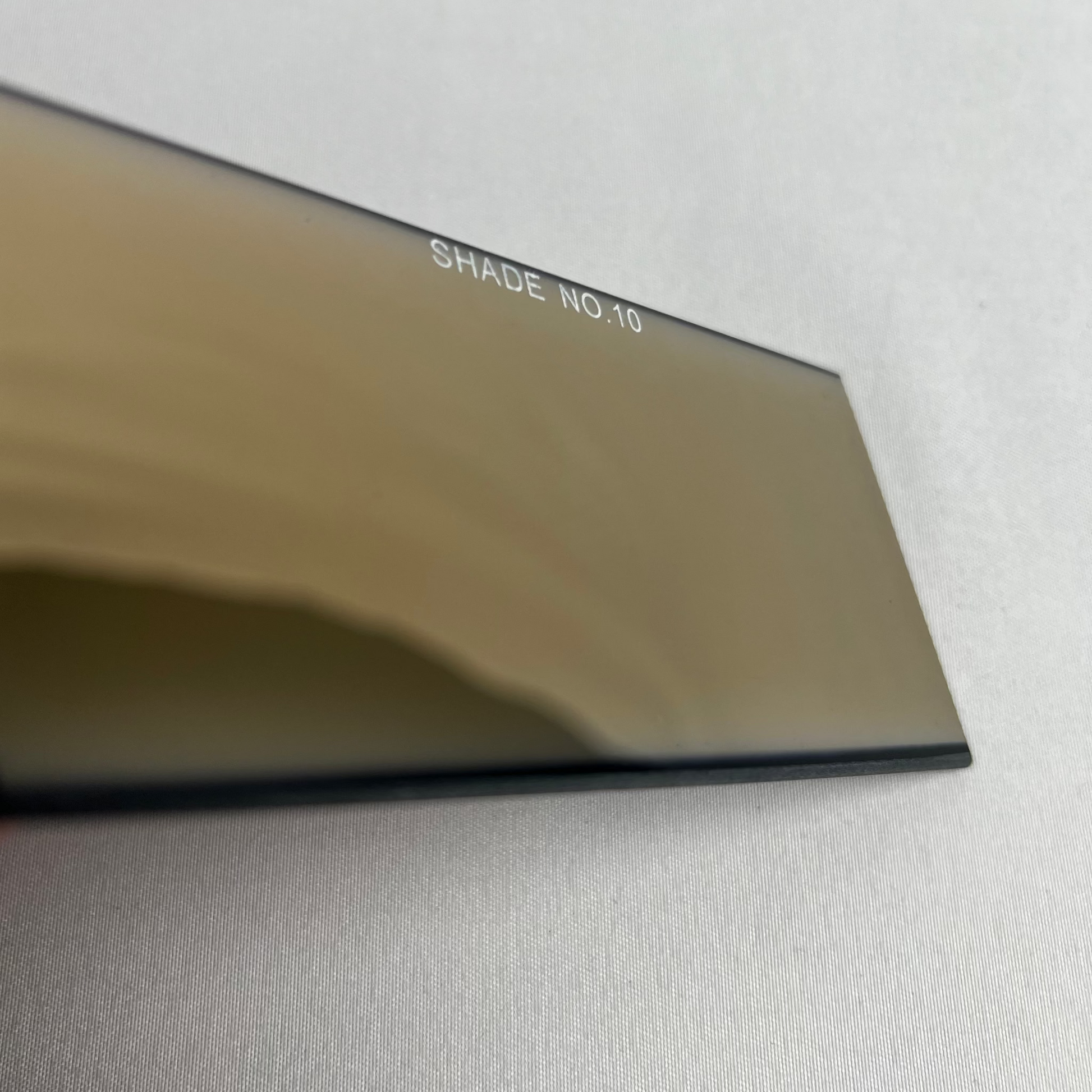 Close-up of a metallic object with 'Shade No 10' text on a light gray background
